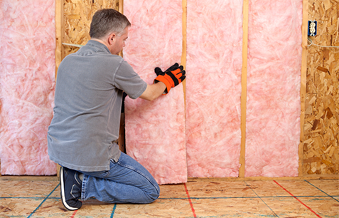 Technician installing pink fiberglass batt insulation in walls