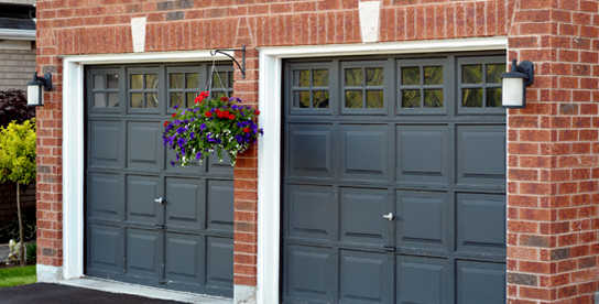 Double garage doors in a brick structure. The doors are painted a dark color with white trim.