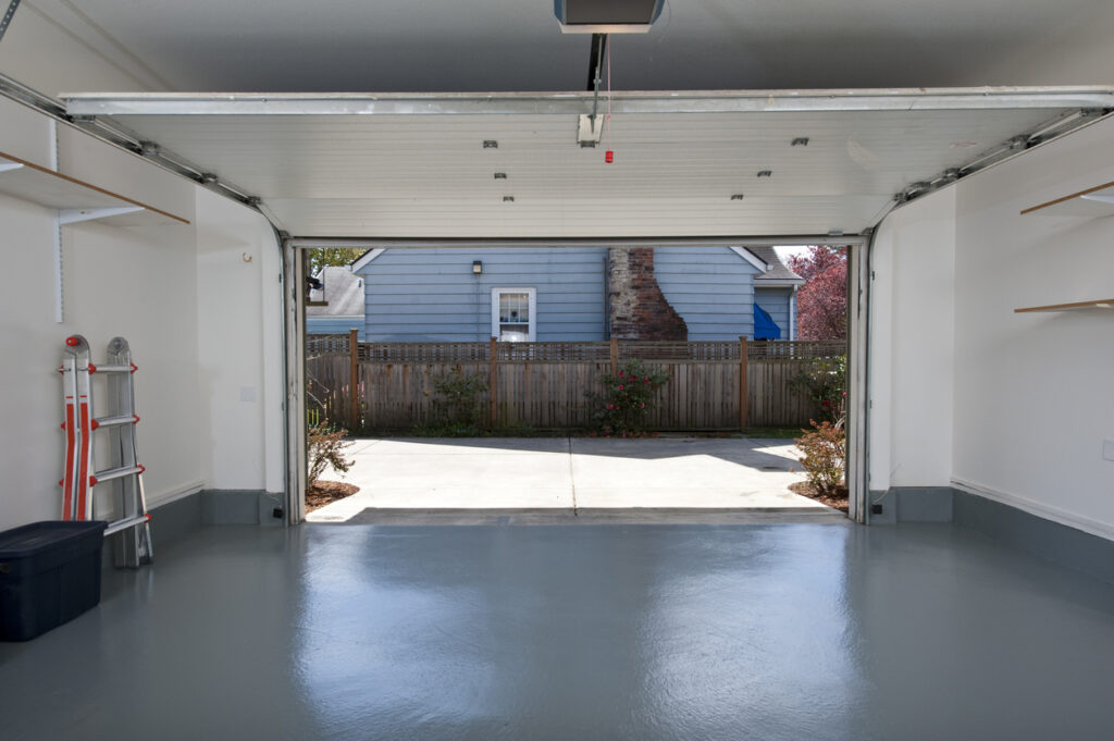 Interior of a clean empty garage with an open garage door. View of driveway and a wooden fence.