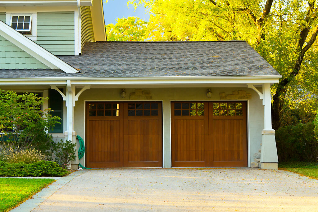 Two woodgrain garage doors with small windows in the top, on a home with light green siding.