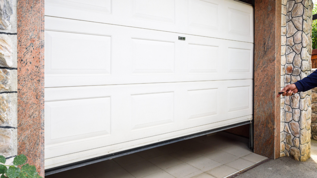Hand pressing garage door opener in front of partially opened garage door